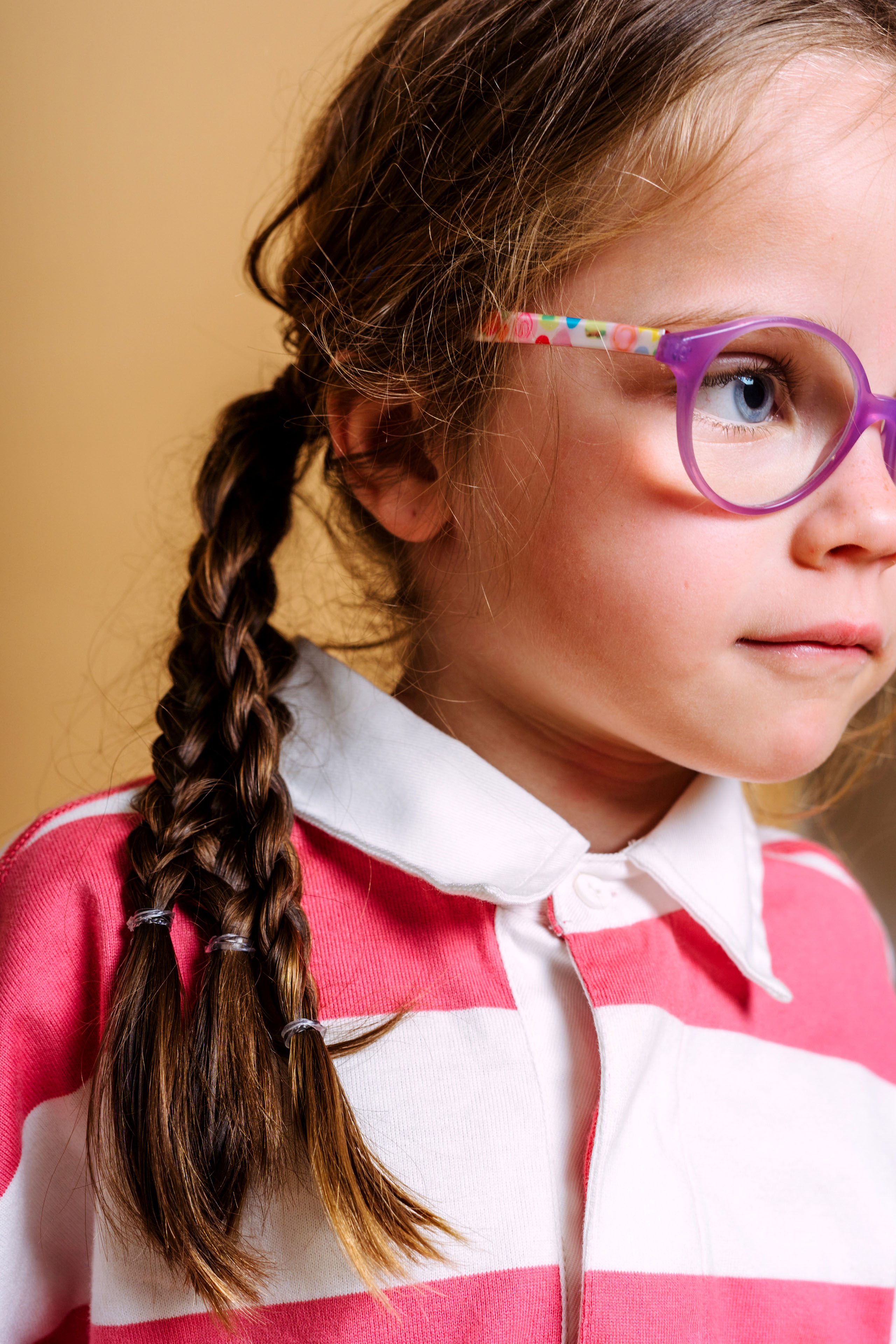 A young girl with braids and purple glasses, looking off to the side.
