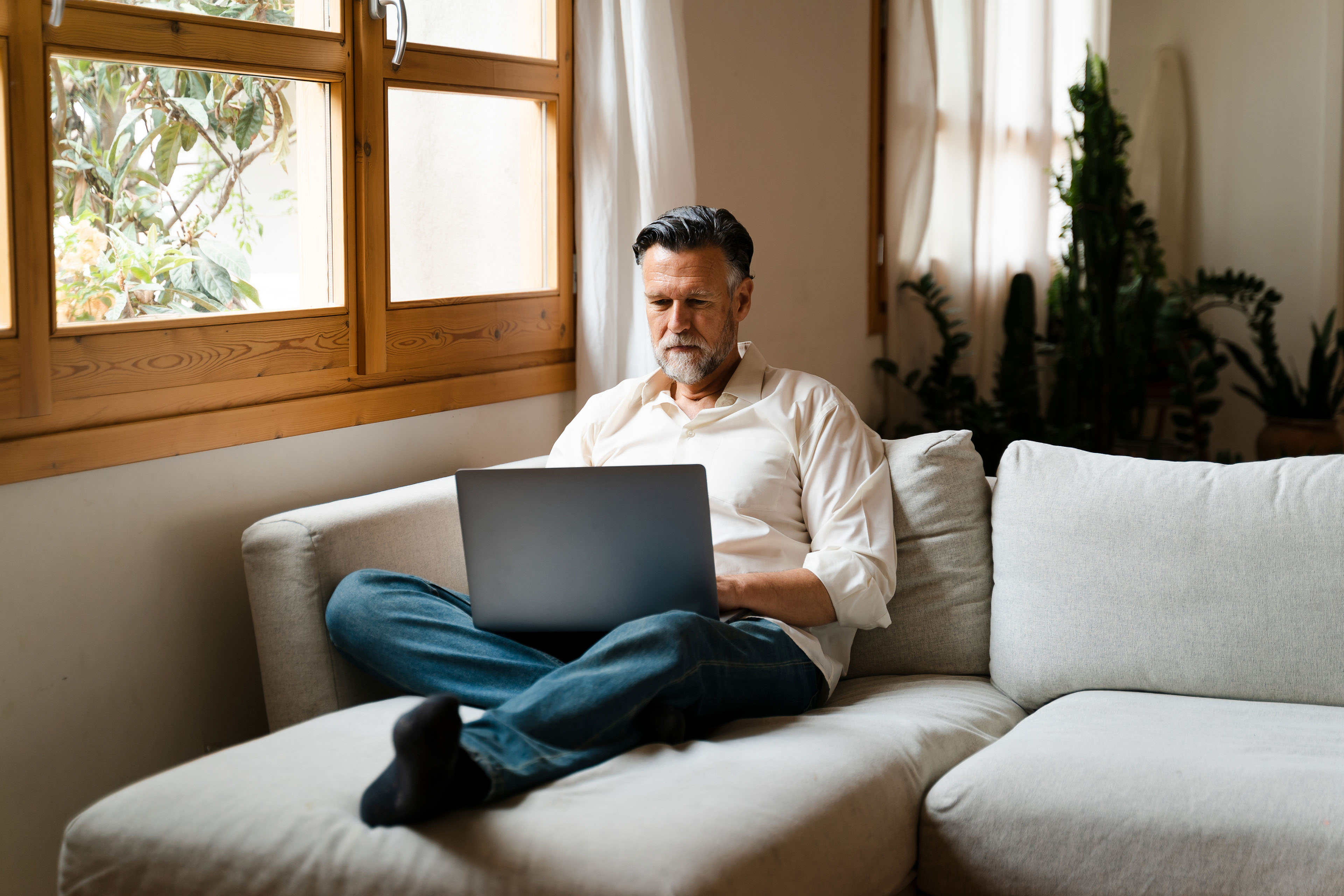 A man sitting cross-legged on a sofa with a laptop.