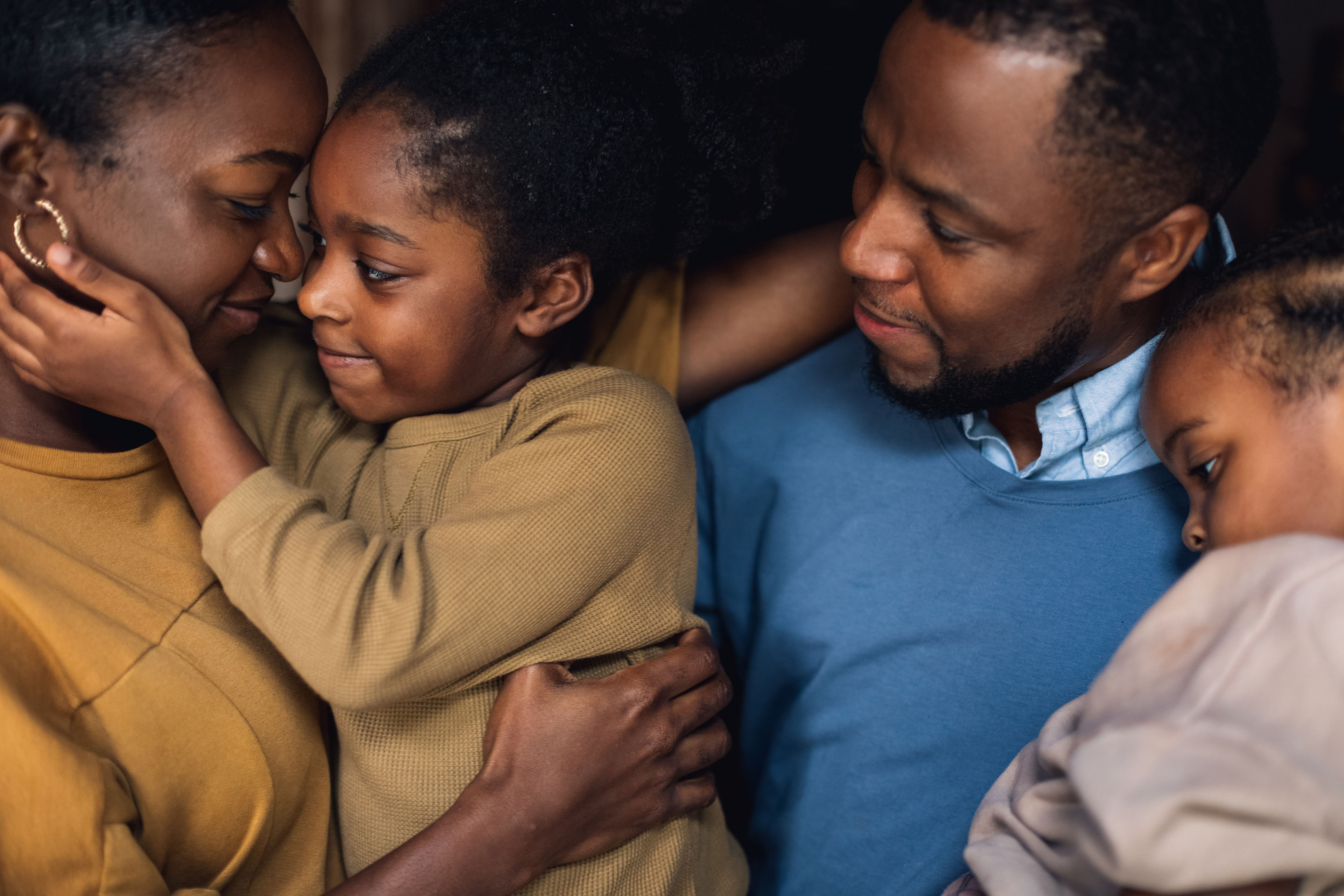Two parents and their young daughters in a close embrace.