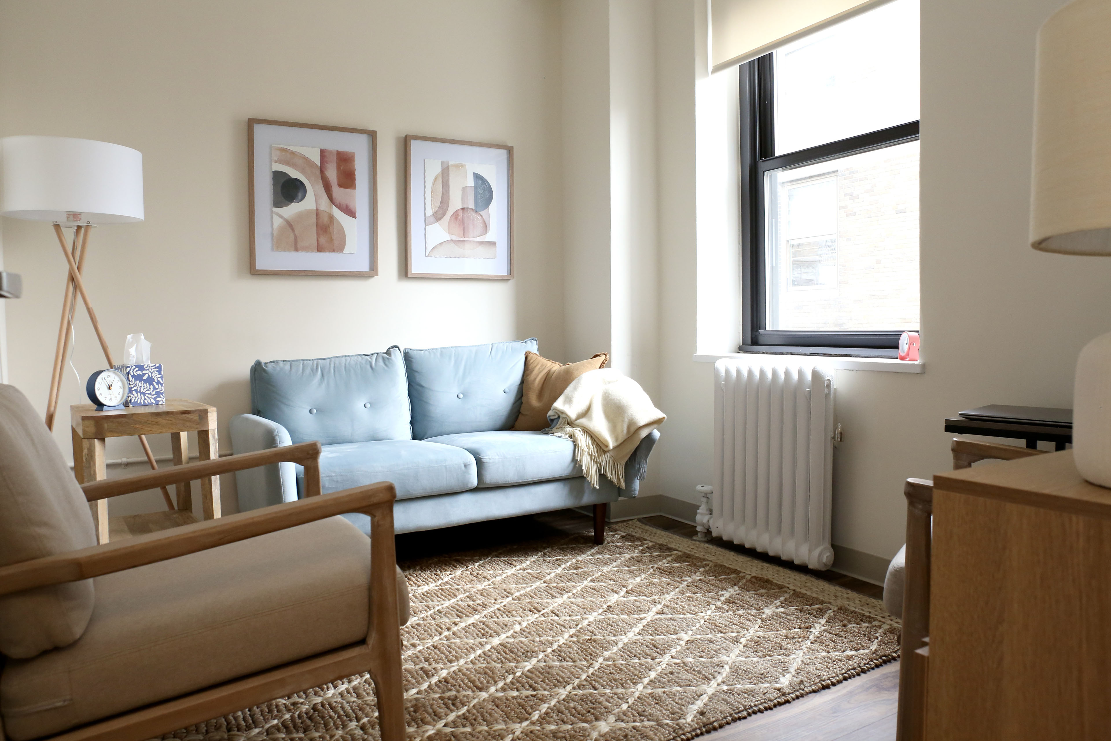 A therapy room with an armchair, a blue sofa and two framed prints.