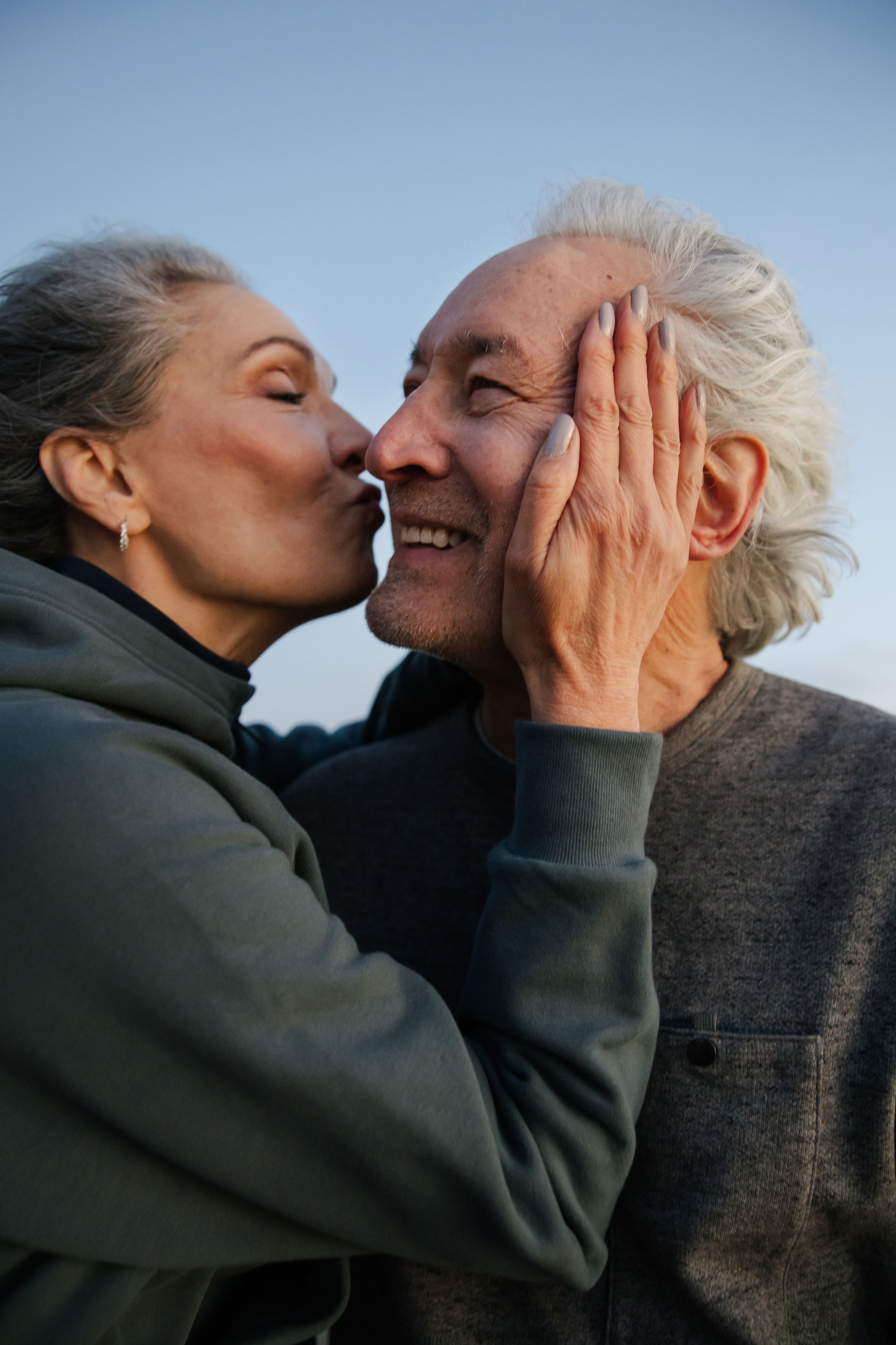An older woman kissing her partner’s cheek as he smiles.