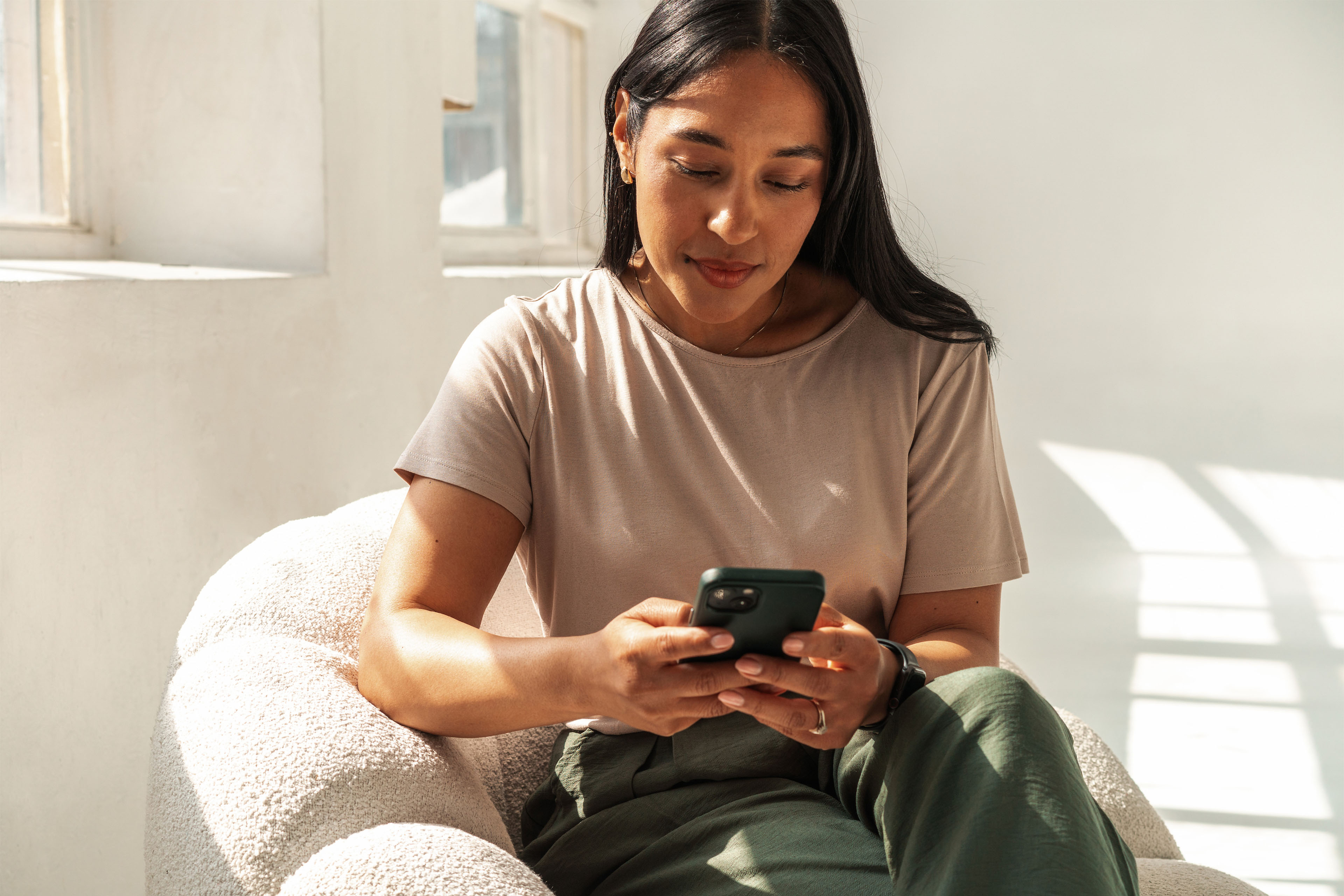 A woman sitting in an armchair, looking at her phone.