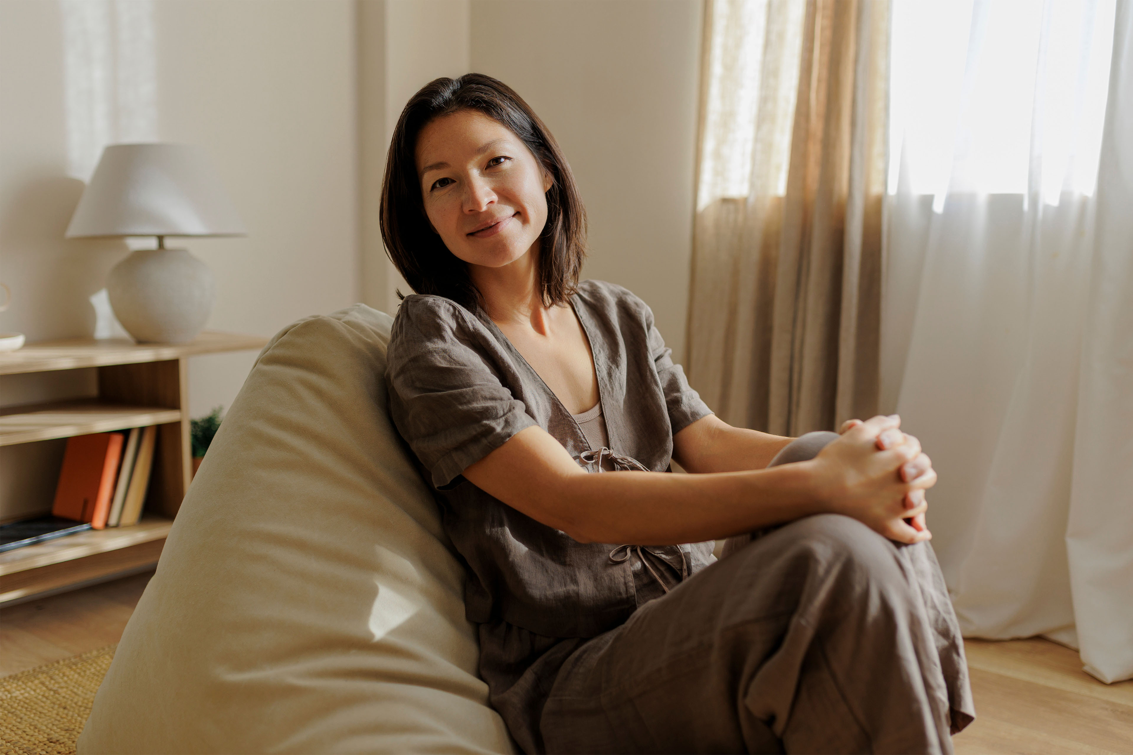 A woman sitting on a large floor cushion in a bright room.